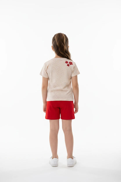 Girl wearing The Nile Luxuries beige polka dot t-shirt with floral appliqué and red shorts, back view.