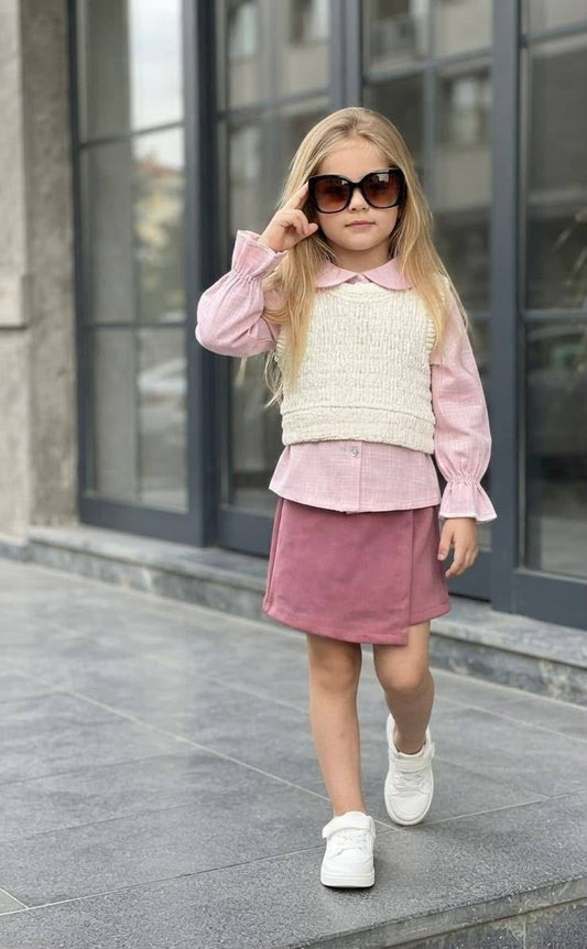 The Nile Luxuries three-piece set featuring a pink ruffled shirt, cream knit vest, and mauve wrap skirt on a girl.
