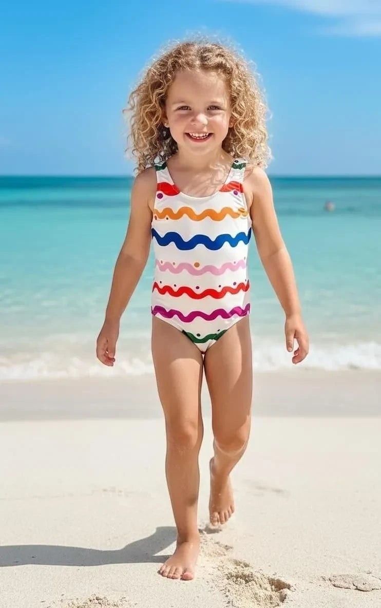 The Nile Luxuries girls' one-piece swimsuit with wavy stripes in red, orange, blue, pink, purple, and polka dots on white.
