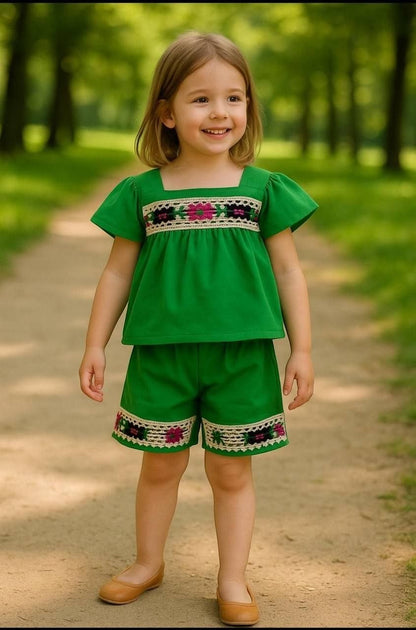 A young girl wearing a green The Nile Luxuries embroidered top and shorts set with floral lace trim in a park.