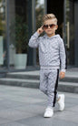 A young boy wearing The Nile Luxuries grey geometric print hoodie and jogger set with black side stripes and sneakers.