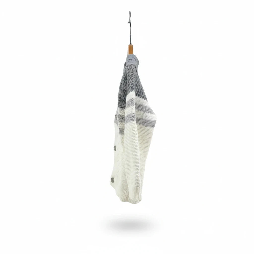 The Nile Luxuries infant knit cardigan in white and grey with button closure hanging on a wooden hanger