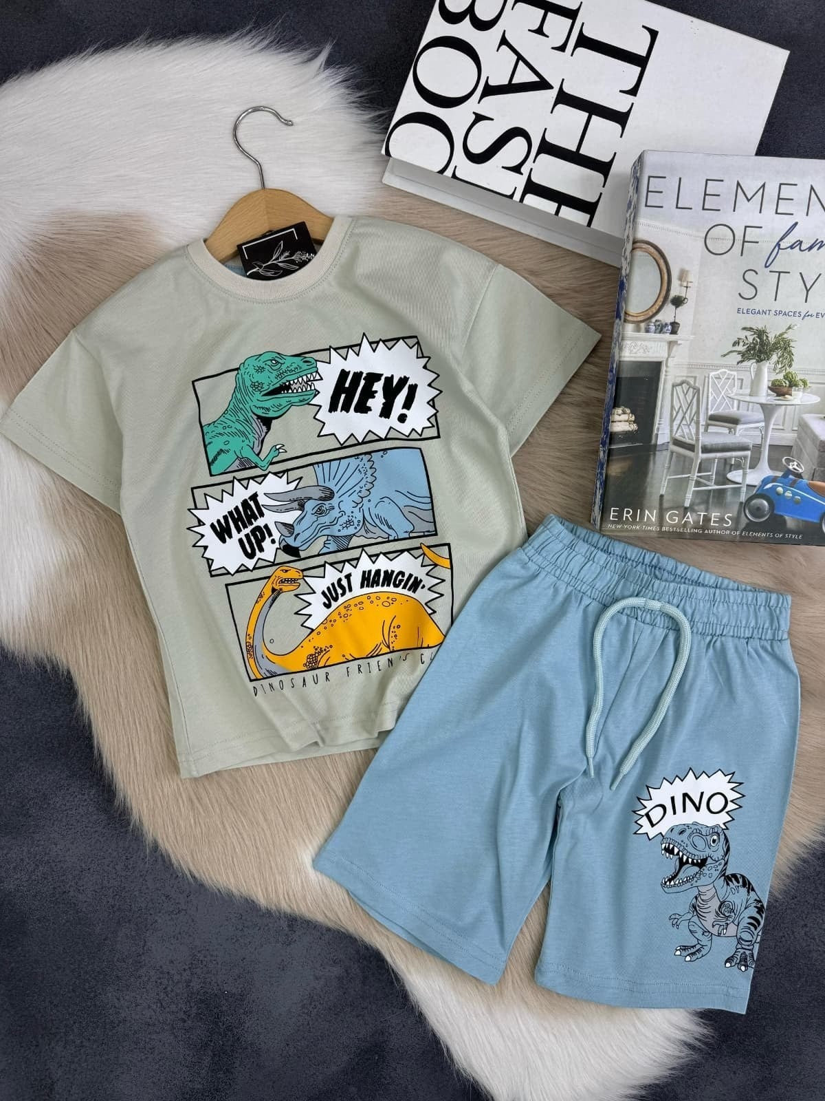 The Nile Luxuries kids light green t-shirt with dinosaur graphics and blue shorts. T-shirt has "HEY!", "WHAT UP!", "JUST HANGIN'" text. Shorts have "DINO" graphic.