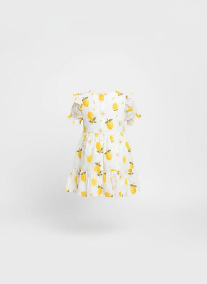 The Nile Luxuries girls white dress with yellow lemon and daisy print, featuring puff sleeves and a tiered skirt.