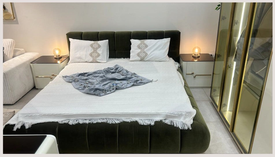 The Nile Luxuries modern bedroom set featuring a plush olive green bed, cream nightstands with gold hardware, and a glass-door wardrobe with interior lighting.