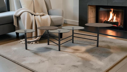 The Nile Luxuries set of 5 modern nesting coffee tables with round wood and smoked glass tops on black metal frames.