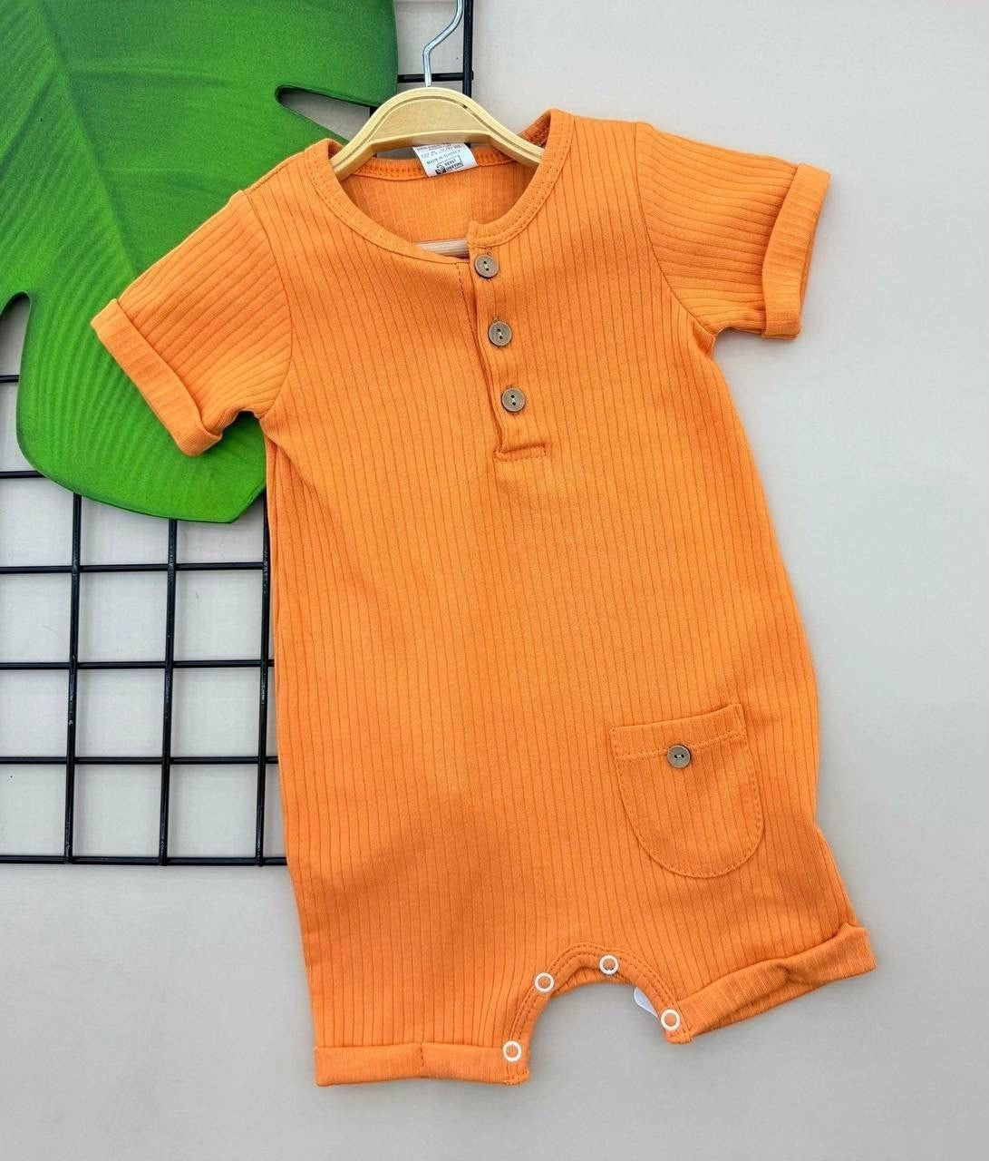 The Nile Luxuries orange ribbed cotton baby romper with a button placket, short sleeves, and a small front pocket.