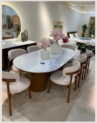 The Nile Luxuries oval marble dining table with eight upholstered chairs. Features a natural marble top and dark wood base.