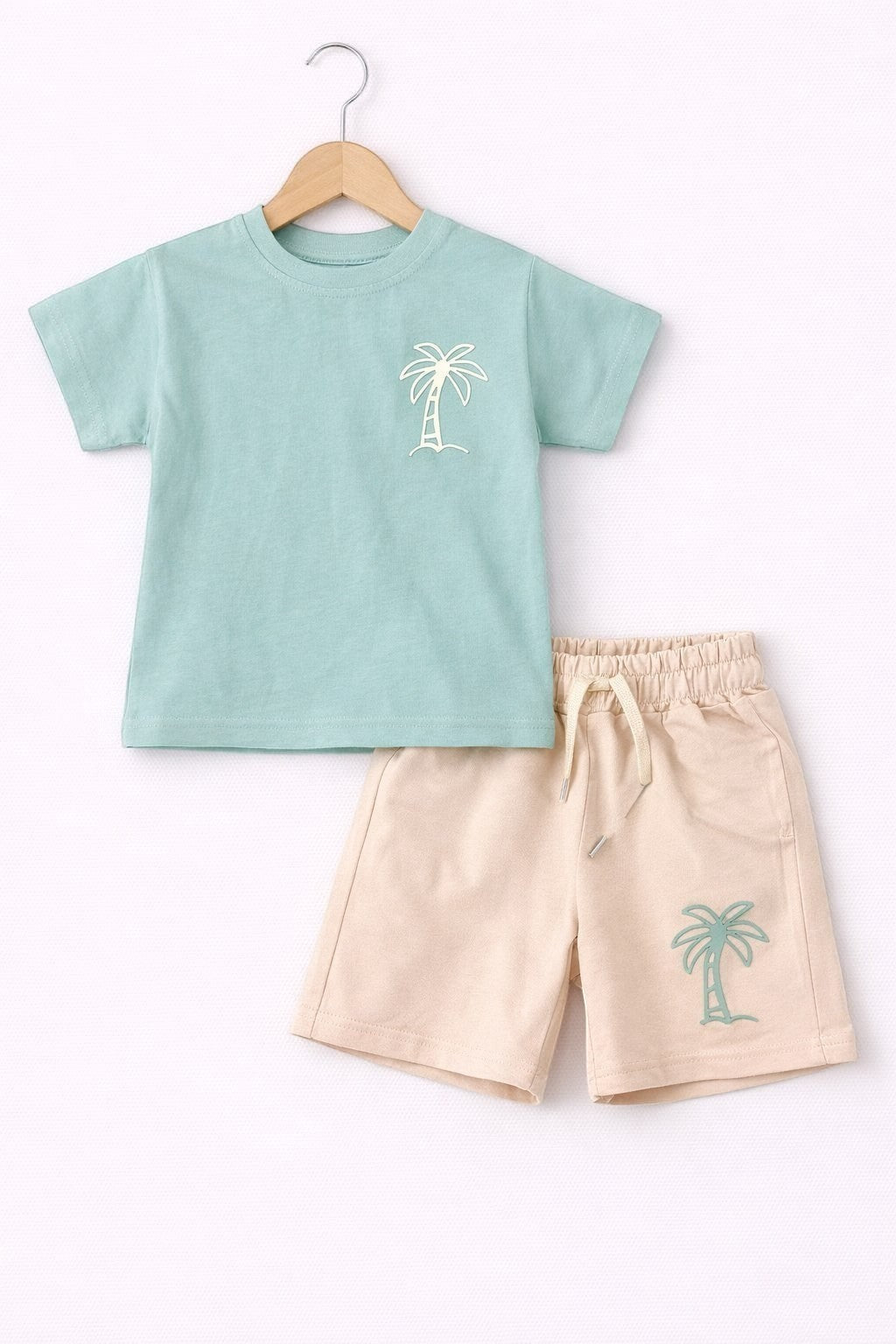The Nile Luxuries children's two-piece set featuring a sage green palm tree t-shirt and beige drawstring shorts.