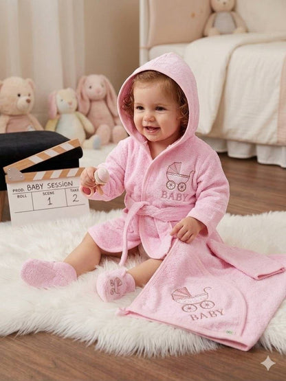 The Nile Luxuries pink hooded baby bathrobe and matching towel set with embroidered baby carriage design on a rug.