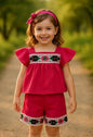 The Nile Luxuries toddler girl wearing a pink flutter-sleeve top and shorts set with floral embroidery and lace trim.