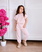 A young girl wearing a The Nile Luxuries light pink short-sleeve hoodie and matching joggers with floral embroidery.