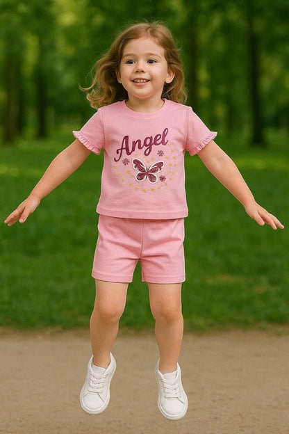 The Nile Luxuries pink girls short set with ruffled sleeves, Angel graphic, and butterfly motif in a park setting.