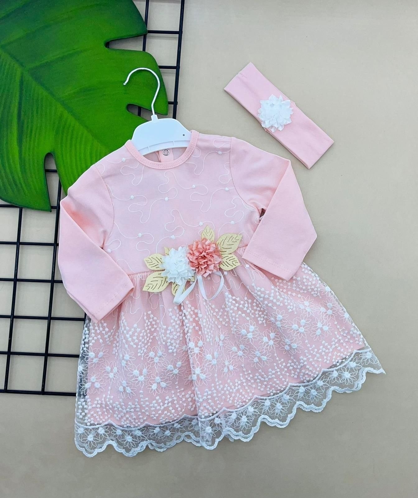 The Nile Luxuries baby girl's pink dress with white lace overlay, floral appliqué, and matching headband. Long sleeves and scalloped hem.