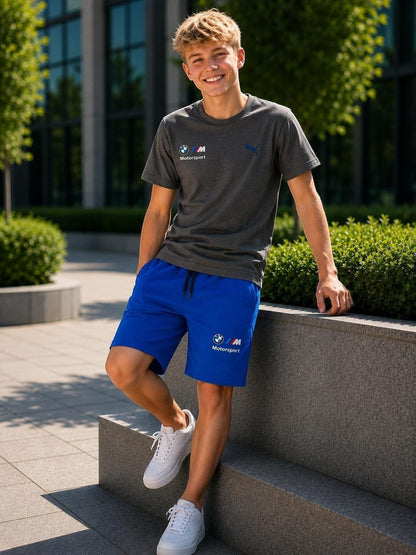 The Nile Luxuries PUMA BMW Motorsport set with a grey crew-neck t-shirt and blue athletic shorts on a smiling model.