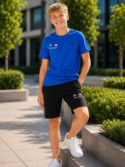 The Nile Luxuries PUMA BMW Motorsport blue crew-neck t-shirt and black athletic shorts worn by a smiling young man.