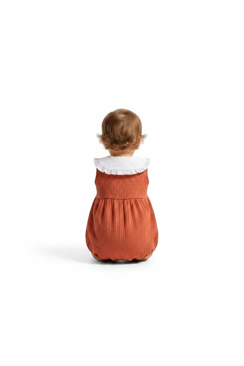 Baby wearing a The Nile Luxuries rust-colored ribbed bubble romper with a white ruffled Peter Pan collar.