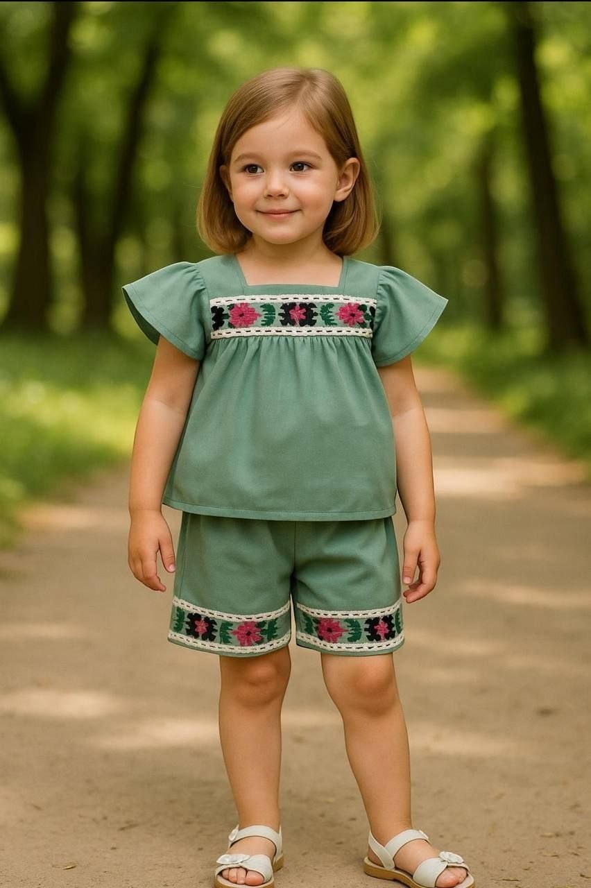The Nile Luxuries toddler girl sage green flutter-sleeve top and shorts set with floral embroidery and lace trim.