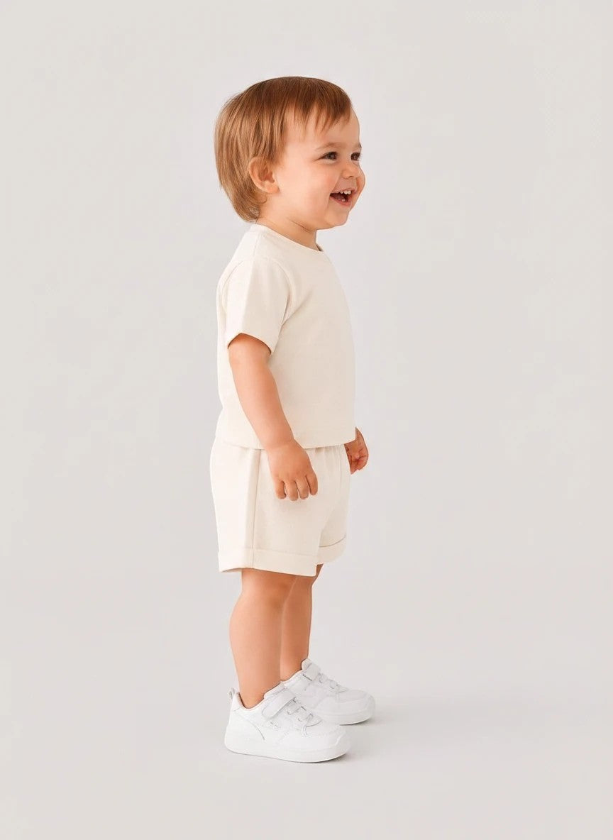 The Nile Luxuries toddler beige short sleeve shirt and shorts set worn by a smiling child in profile view.