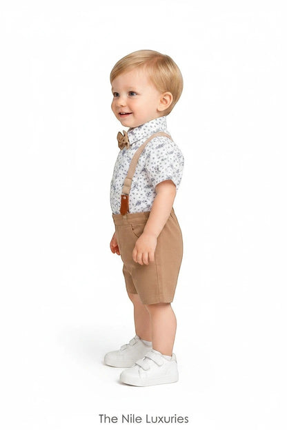 Toddler boy wearing The Nile Luxuries formal outfit with floral shirt, tan shorts, bow tie, and suspenders.