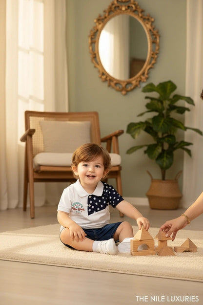 Toddler boy wearing a The Nile Luxuries white color-blocked polo with star print and denim shorts playing with blocks.