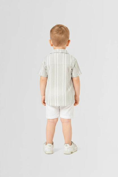 Toddler boy wearing The Nile Luxuries sage striped shirt and white shorts set, viewed from the back.