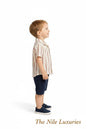 Toddler boy wearing The Nile Luxuries striped button-down shirt and navy shorts, standing against a white background.