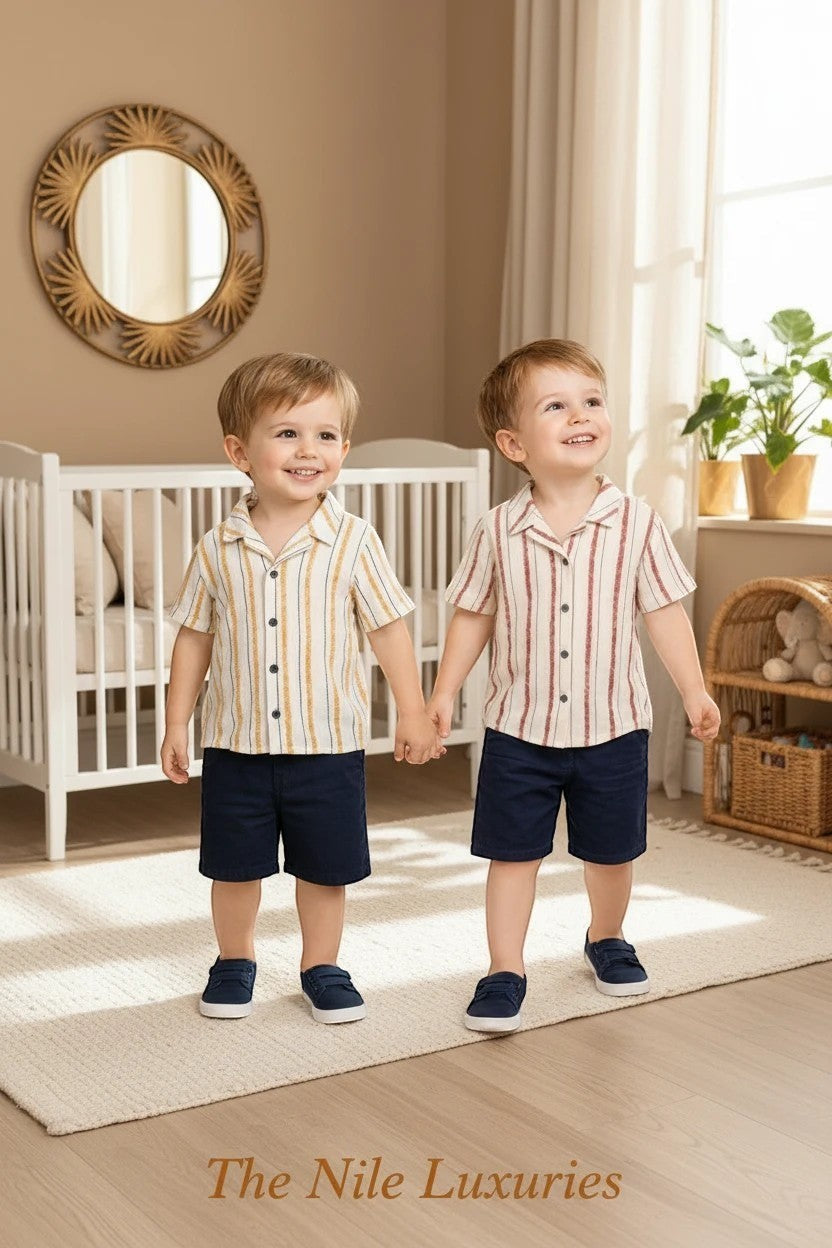 Two toddlers wearing The Nile Luxuries striped button-down shirts and navy shorts in a bright, modern nursery.