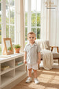 Toddler boy wearing a The Nile Luxuries sage and white striped button-down shirt and white shorts in a bright room.