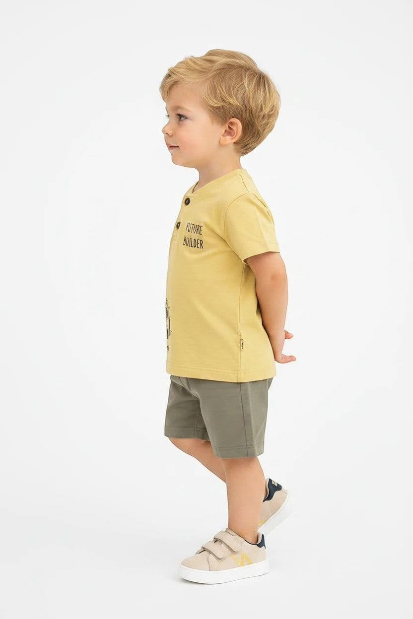 Toddler boy wearing a yellow The Nile Luxuries graphic henley t-shirt and olive shorts against a white background.