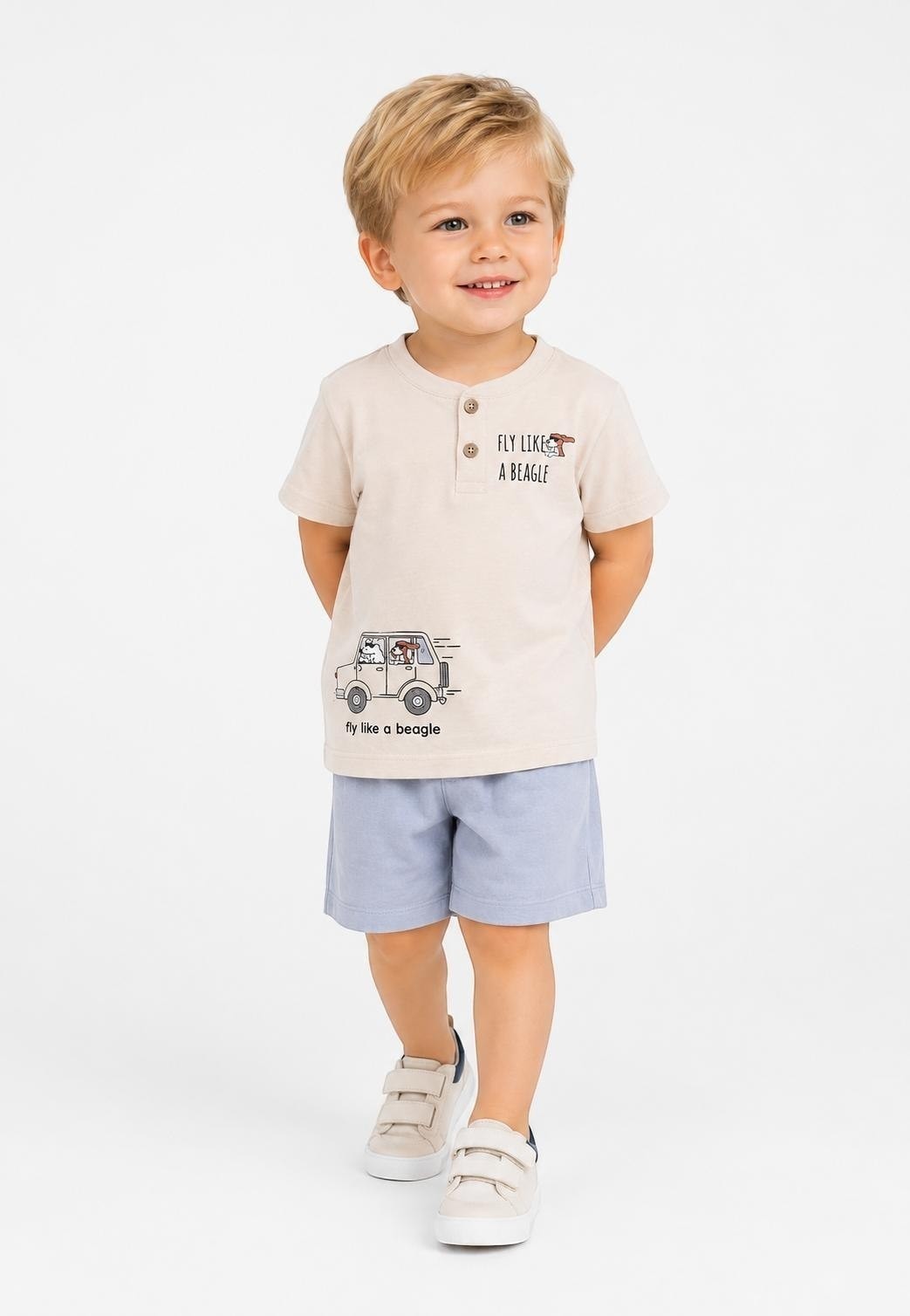 Toddler boy wearing a beige The Nile Luxuries graphic henley t-shirt with a beagle car print and blue shorts.