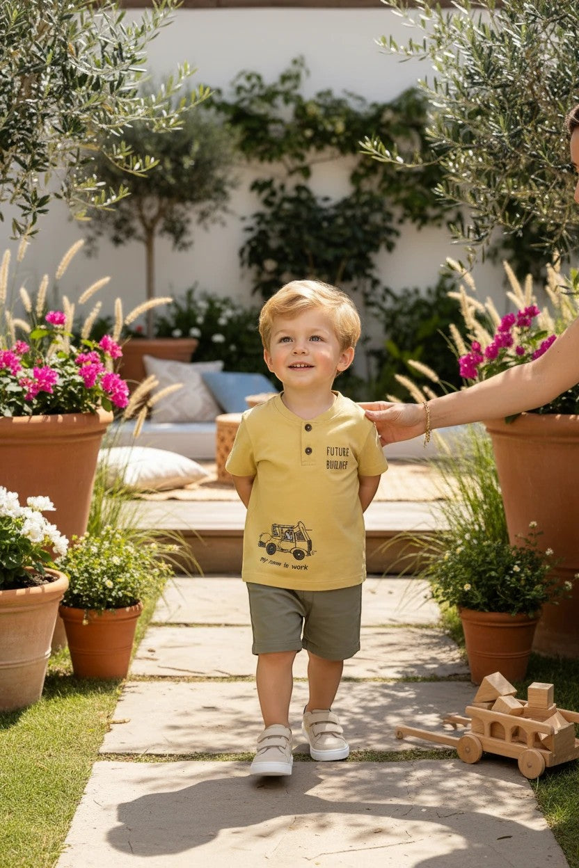 Toddler boy wearing a mustard yellow The Nile Luxuries henley t-shirt with graphic print in a sunny garden setting.