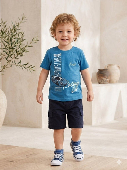 The Nile Luxuries toddler boy wearing a blue sports car graphic t-shirt and navy blue cargo shorts in a bright room.