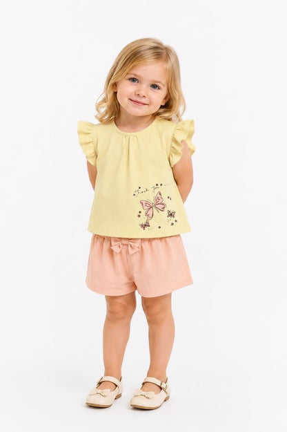 Toddler girl wearing The Nile Luxuries yellow flutter sleeve top with butterfly print and peach shorts with bow.