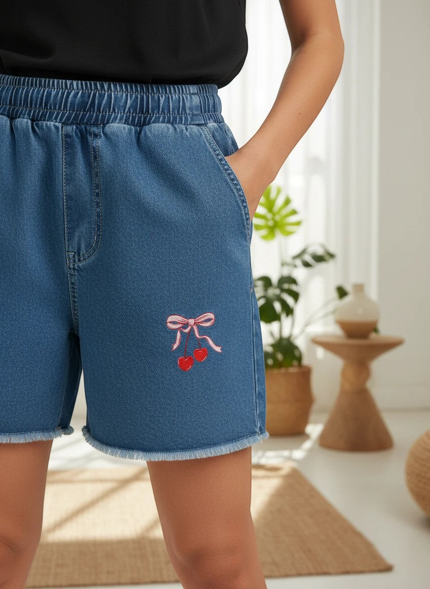 The Nile Luxuries toddler denim shorts with elastic waistband, frayed hem, and embroidered cherry and bow detail.