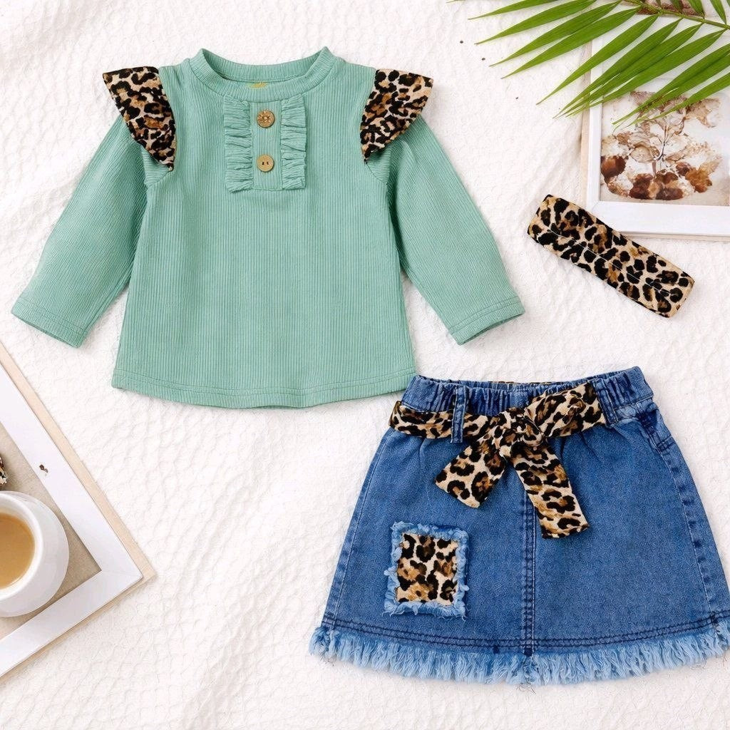 The Nile Luxuries toddler girl outfit with a green ribbed top, denim skirt, leopard print belt, and headband.
