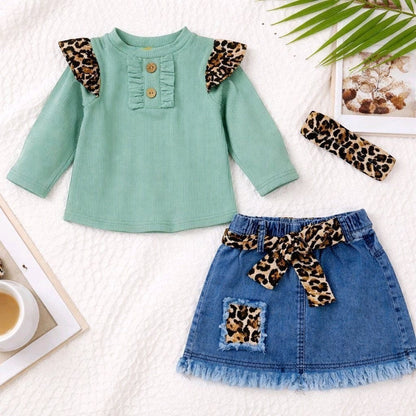 The Nile Luxuries toddler girl outfit with a green ribbed top, denim skirt, leopard print belt, and headband.