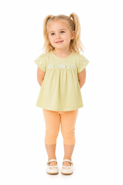 Toddler girl wearing The Nile Luxuries light green embroidered top and peach capri leggings on a white background.