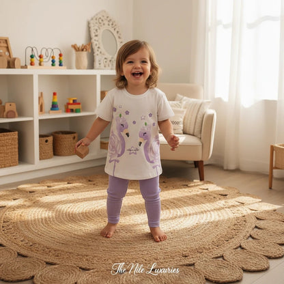 Toddler girl wearing The Nile Luxuries white flamingo graphic t-shirt and purple ribbed leggings in a bright playroom.