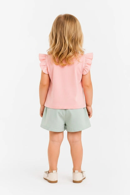 Toddler girl wearing The Nile Luxuries pink flutter sleeve top and sage green shorts set with white shoes