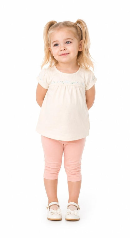 Toddler girl wearing The Nile Luxuries cream embroidered top and pink capri leggings against a white background.