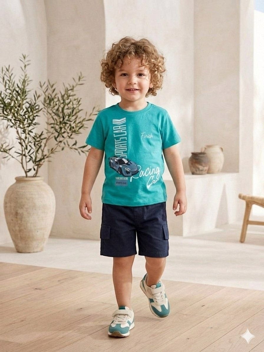The Nile Luxuries toddler boy wearing a teal graphic sports car t-shirt and navy blue cargo shorts in a bright room.