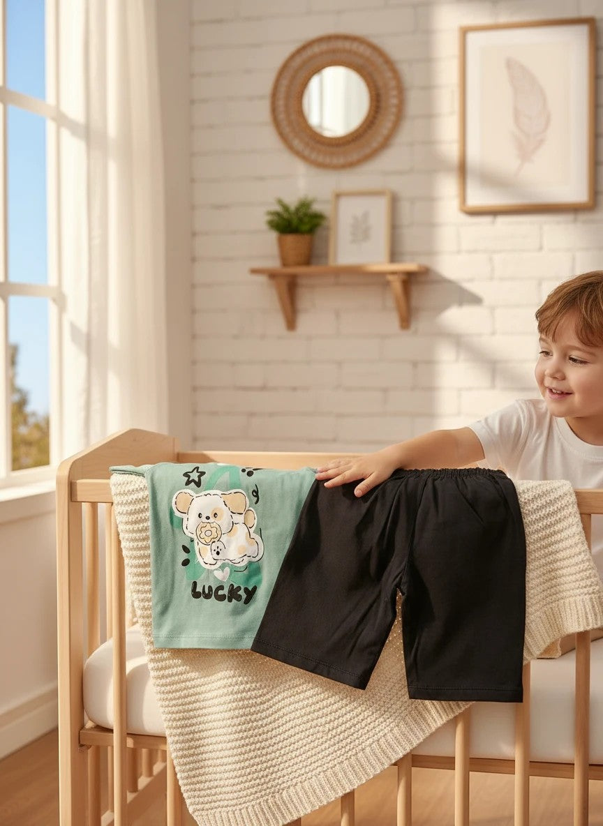 The Nile Luxuries toddler set with a sage green puppy graphic t-shirt and black shorts resting on a wooden crib.
