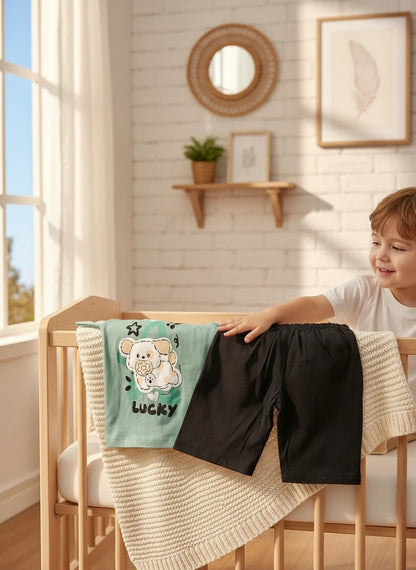 The Nile Luxuries toddler set with a sage green puppy graphic t-shirt and black shorts resting on a wooden crib.