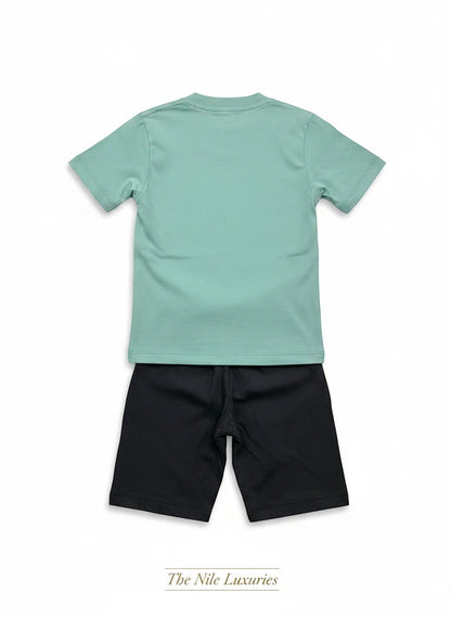 The Nile Luxuries toddler two-piece set featuring a sage green short-sleeved t-shirt and black shorts, back view.