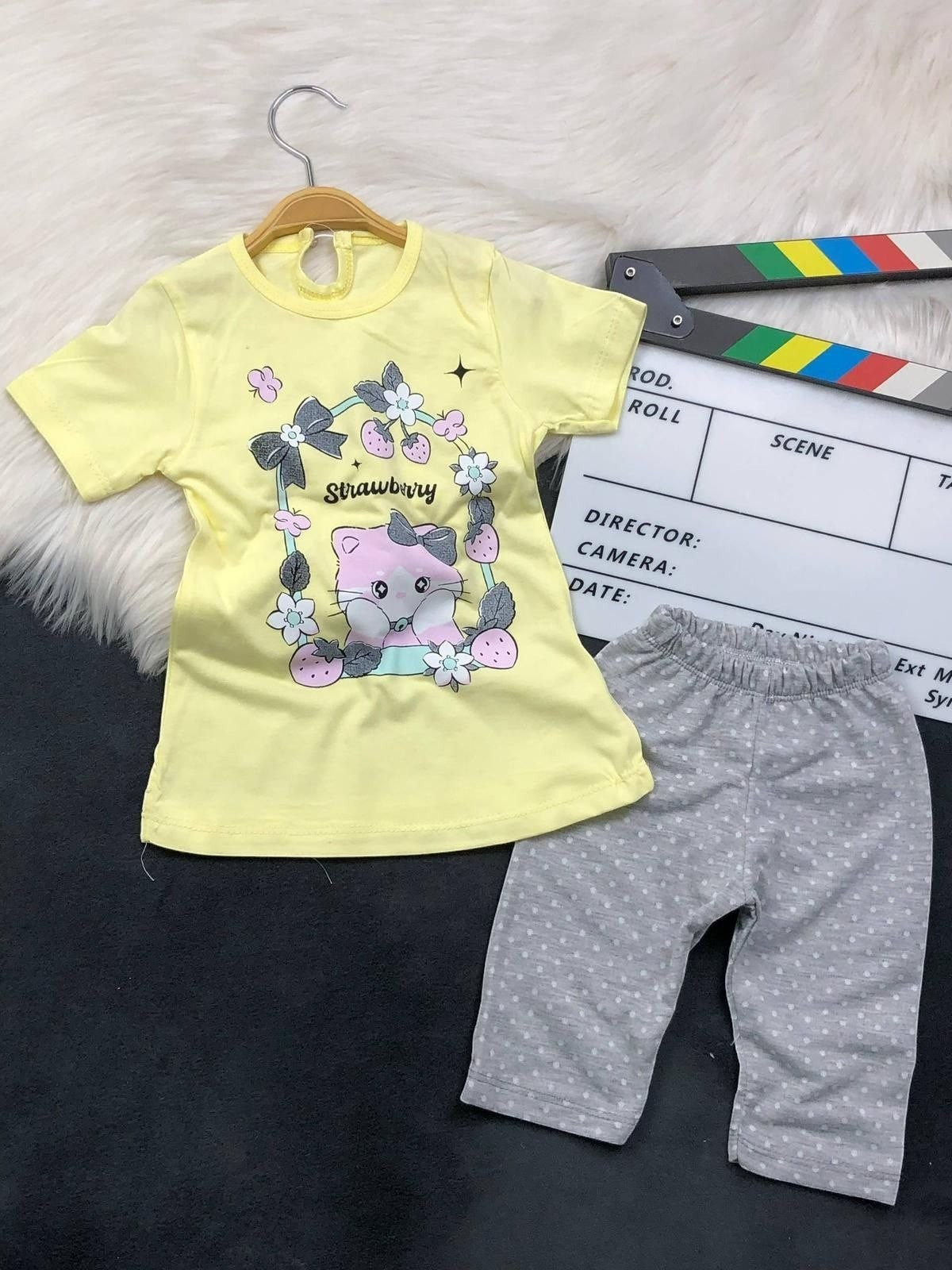 The Nile Luxuries toddler set with a yellow kitten graphic t-shirt and grey polka dot pants on a white faux fur rug.