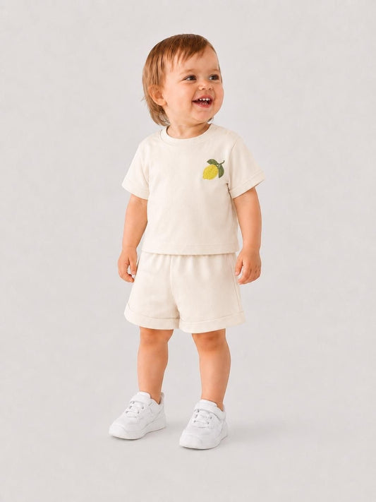 Toddler wearing The Nile Luxuries cream short sleeve shirt and shorts set with lemon embroidery and white sneakers.