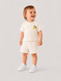 Toddler wearing The Nile Luxuries cream short sleeve shirt and shorts set with lemon embroidery and white sneakers.
