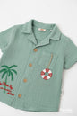 The Nile Luxuries sage green muslin toddler shirt with palm tree embroidery and nautical lifebuoy charm detail.