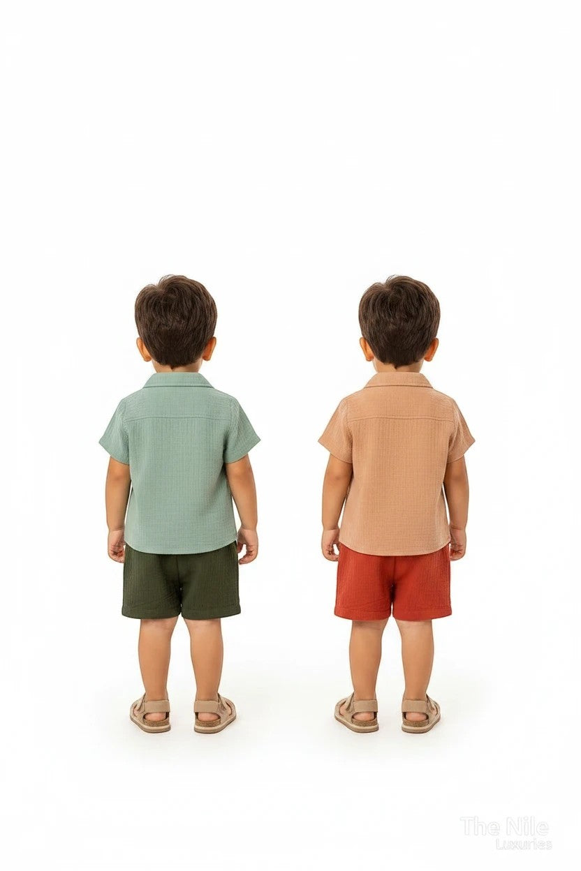 Two toddlers wearing The Nile Luxuries muslin shirt and shorts sets in sage green and earthy terracotta tones.